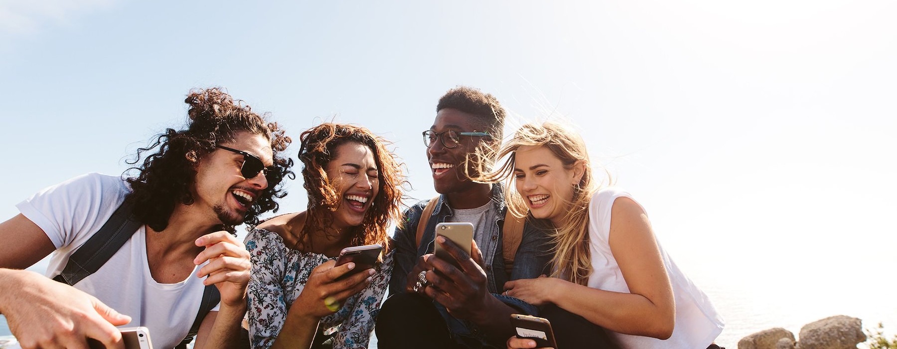 a group of friends sit outside laughing over their cell phones